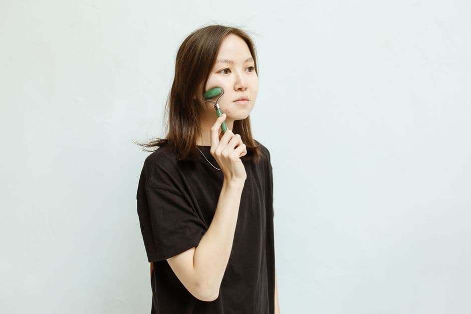 Ảnh minh hoạ — Asian woman using jade roller for facial massage and beauty routine indoors.