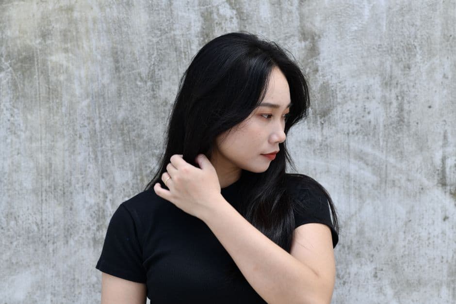 Ảnh minh hoạ — Profile of a woman with long hair touching her face in front of a concrete wall.