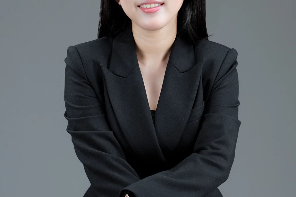 Ảnh minh hoạ — Phụ nữ châu Á trưởng thành mặc blazer, cười thân thiện điềm đạm, nền studio sạch