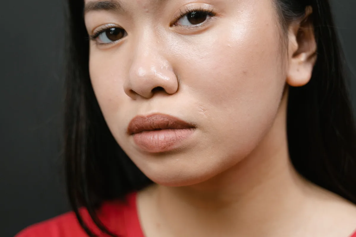 Imagen ilustrativa — Una mujer asiática adulta con top rojo de cuello redondo y piel natural sobre un fondo gris limpio