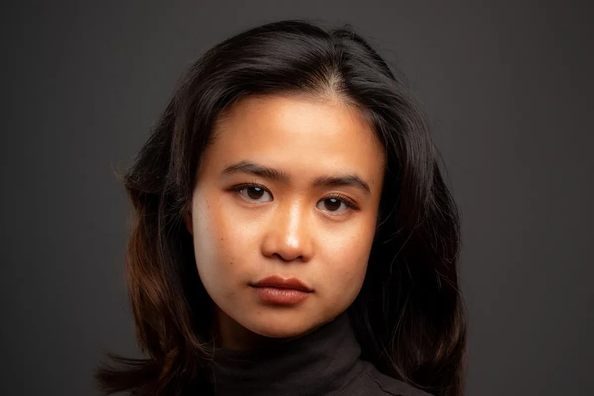 Illustrative image — An adult Asian woman in a black turtleneck, a studio portrait on a grey background with clear skin